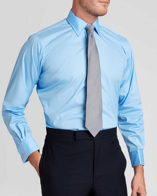 Man wearing blue shirt and tie with suit trousers against plain cream background