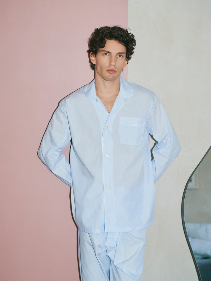 Man wearing sky blue pyjamas stood against a pink and cream block wall