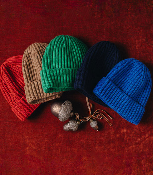 Four knit hats in red, brown, green, and blue on a red background.