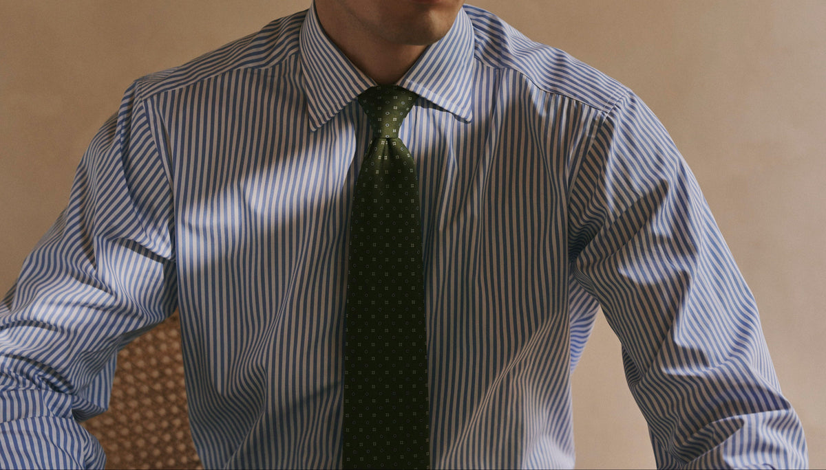 A man wearing a blue and white vertically striped dress shirt with a dark green patterned tie, shown from the chest up against a warm beige background.