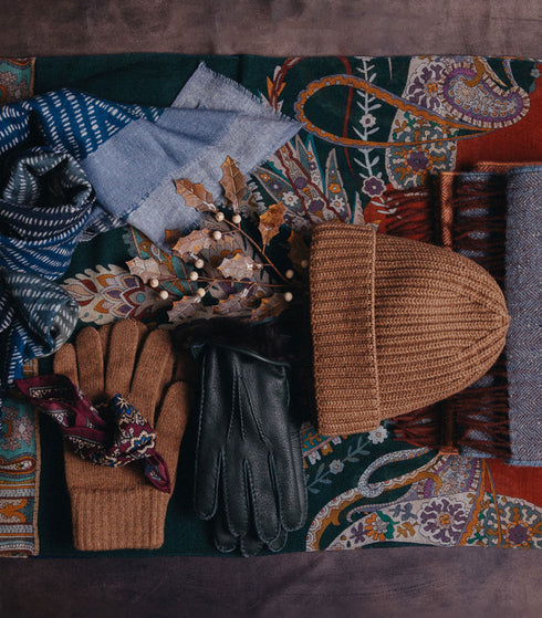 Collection of winter accessories including gloves, a beanie, and a scarf on a patterned fabric background.
